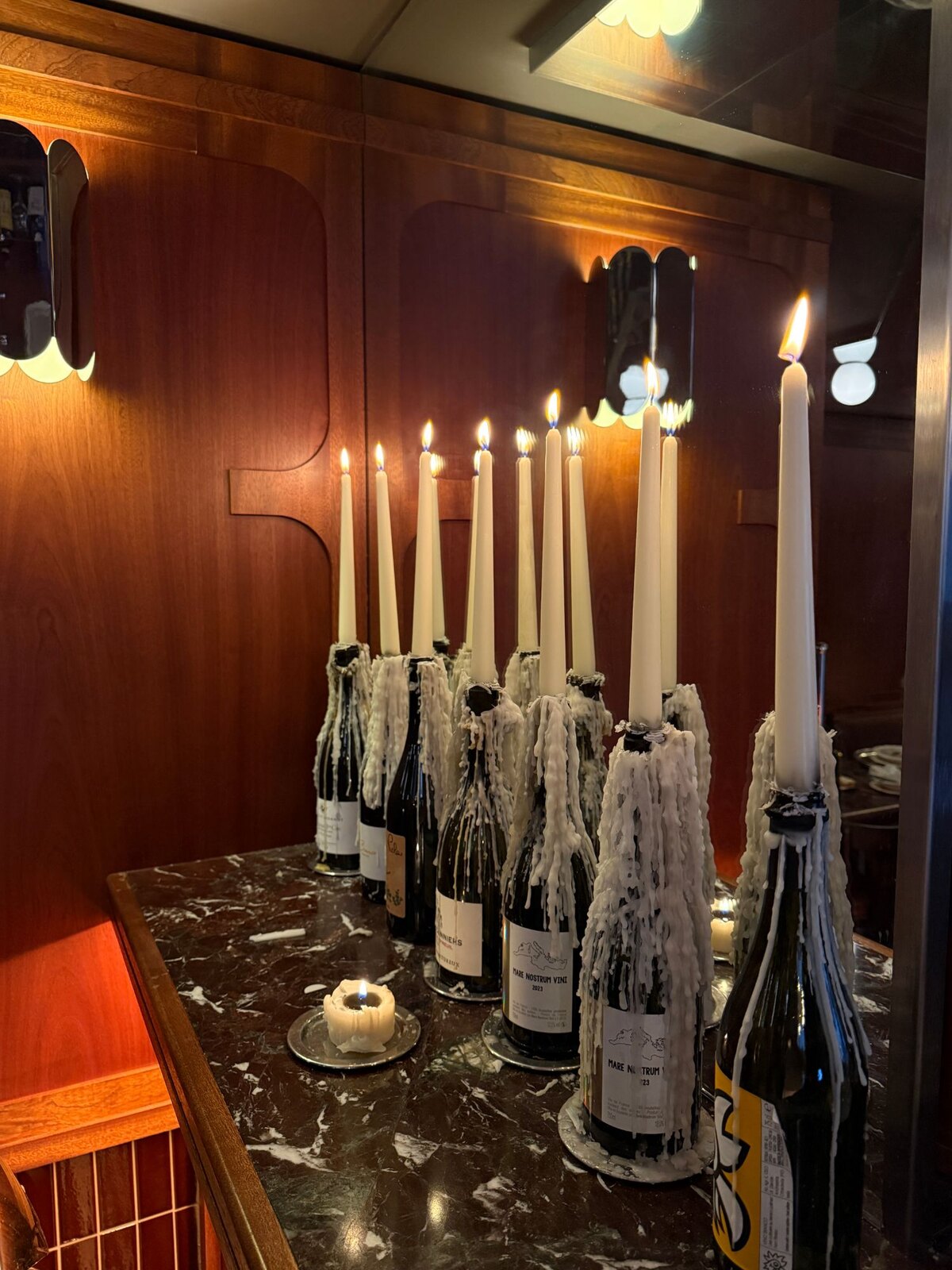 Bougies fichées dans des bouteilles de vin, coulées de cire et boiseries en acajou, au bar de Monica